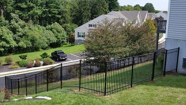 Black metal fence along a sloped lawn overlooking a road and houses.