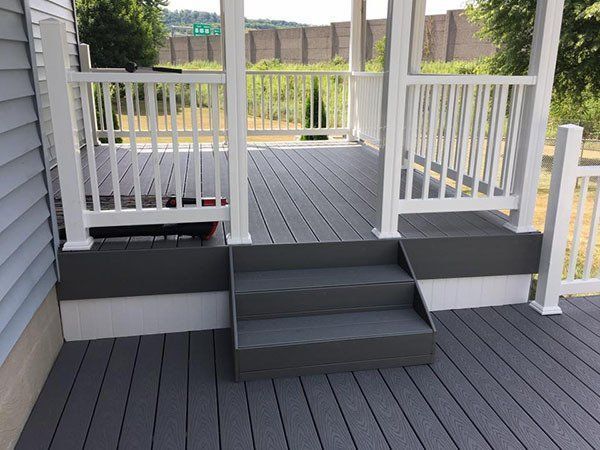 White porch with gray steps and railing, leading to a deck overlooking a backyard fence.