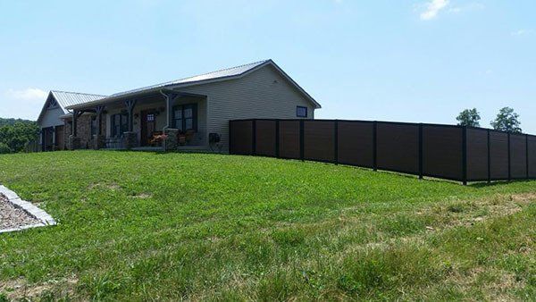 Single-story house on a grassy hill with a long dark fence under a clear sky.