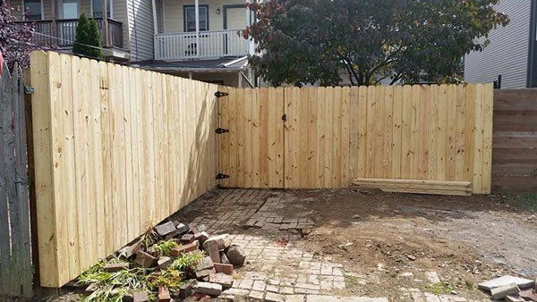 Backyard with new wooden fence along the left and back, and a paved patio with dirt in the foreground.