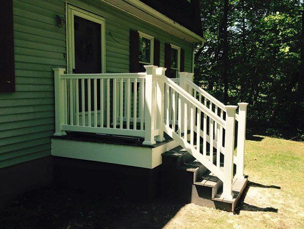 Green house porch with white railing and wheelchair ramp leading down to a grassy yard