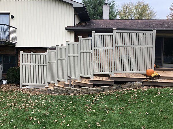 House exterior with a gray privacy fence, wooden steps, and a small orange pumpkin on the deck.