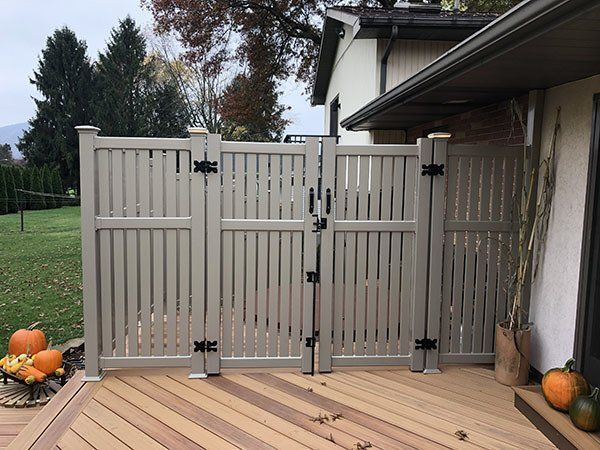 Beige folding gate on a wooden deck beside a house, with pumpkins and a grassy yard beyond.