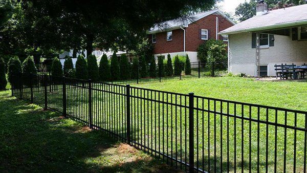 Black metal fence along a grassy yard with houses and trees in the background.