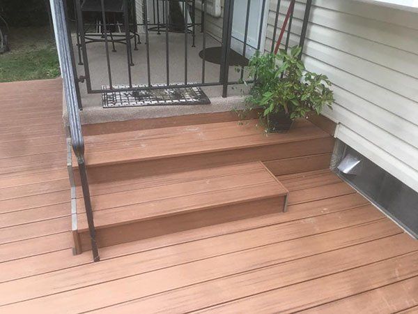 Wooden deck with two steps leading to a small porch, black railing, and a potted plant beside the door.