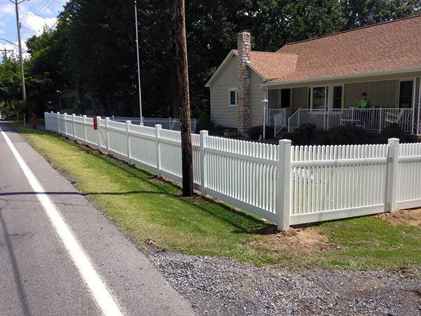 White picket fence along a roadside beside a tan house with a porch and red roof