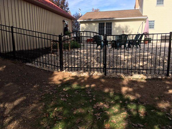 Backyard patio with black metal fence, outdoor table and chairs, beside tan buildings and a dirt path