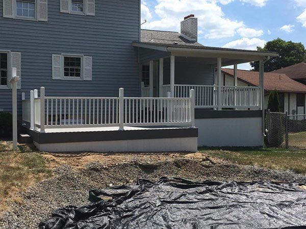 Blue house with a white porch ramp and railing, black tarp on the ground, and a small covered porch.