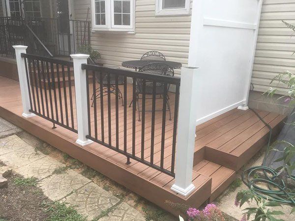 Small wooden deck with black railings and white posts beside a house, with steps on the right