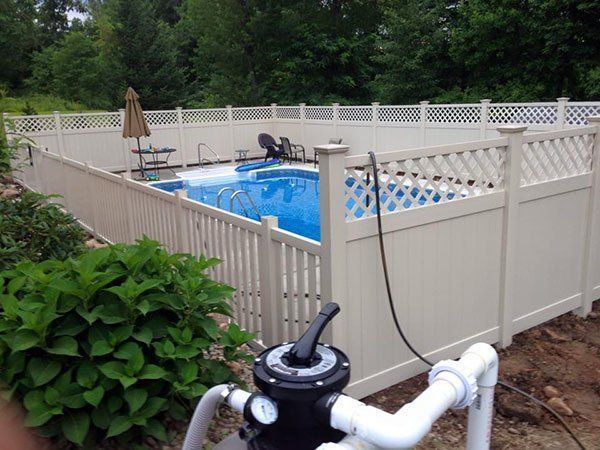 Backyard swimming pool enclosed by a white fence, with pool equipment in the foreground.
