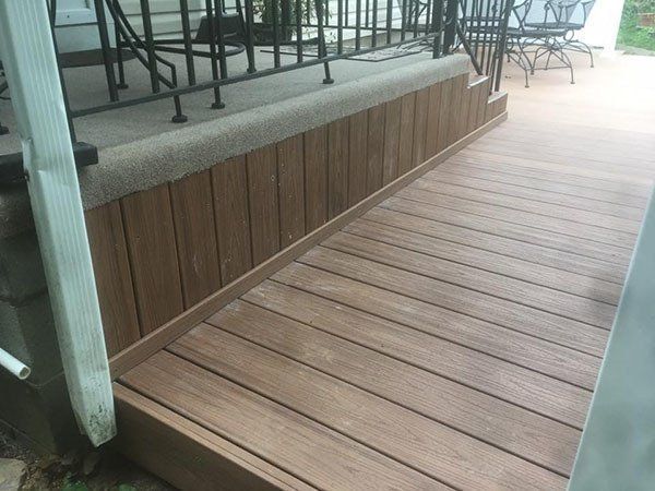 Wooden deck walkway beside a raised patio with metal railings and outdoor chairs