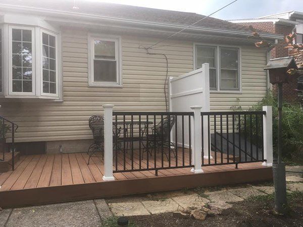 Back porch deck with white railing and black balusters on a beige house, viewed from the yard