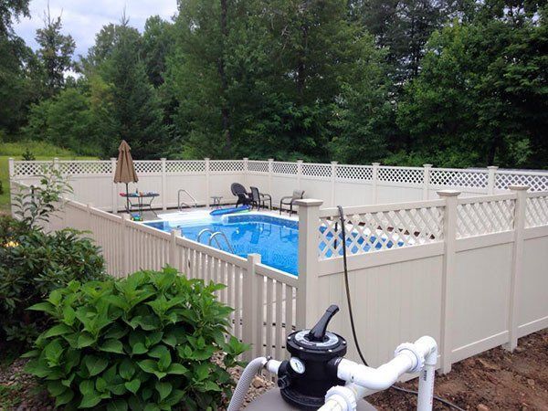Backyard above-ground pool enclosed by a white fence, with patio furniture and greenery.