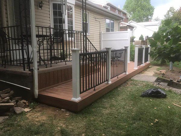 Small wooden porch deck with black railings and white posts beside a beige house.