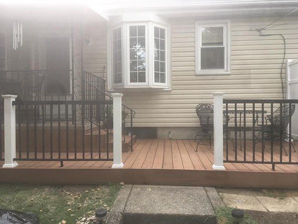Front porch of a beige house with black railings, white posts, and a bay window, viewed from the yard.