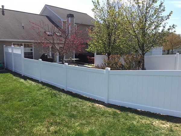 White fence around a backyard with a house and trees in the background