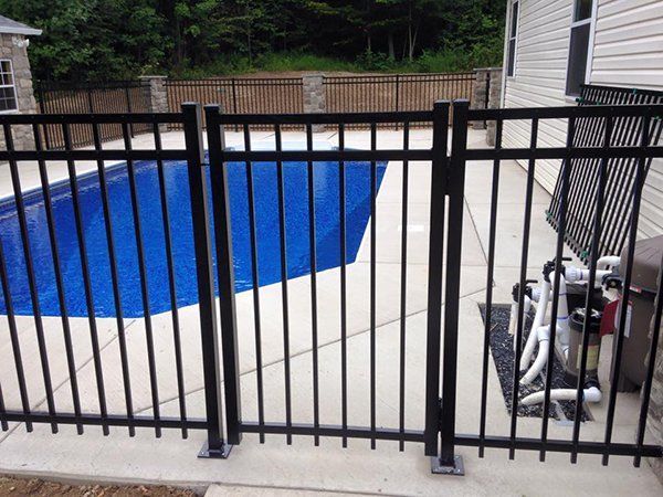 Backyard patio with a blue-covered pool behind a black metal fence, grill on the right.