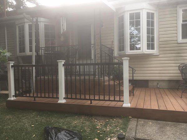 Front porch with black railing, white columns, and wooden deck on a beige house