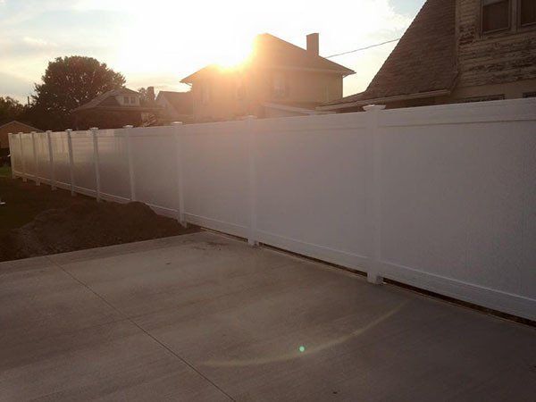Sunlit backyard with a white privacy fence and concrete patio at sunset