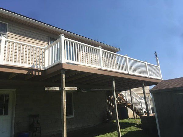 Raised backyard deck with white railings over a shaded patio beneath a beige house