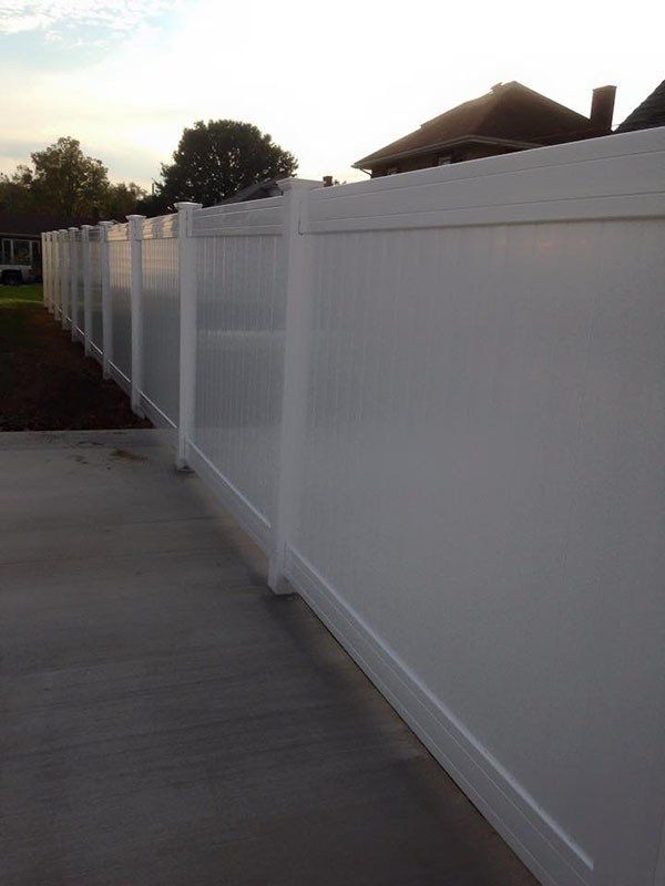 White vinyl fence beside a concrete walkway in a residential yard at dusk