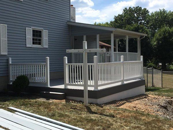 White-railed wooden porch deck attached to a gray house beside a grassy yard