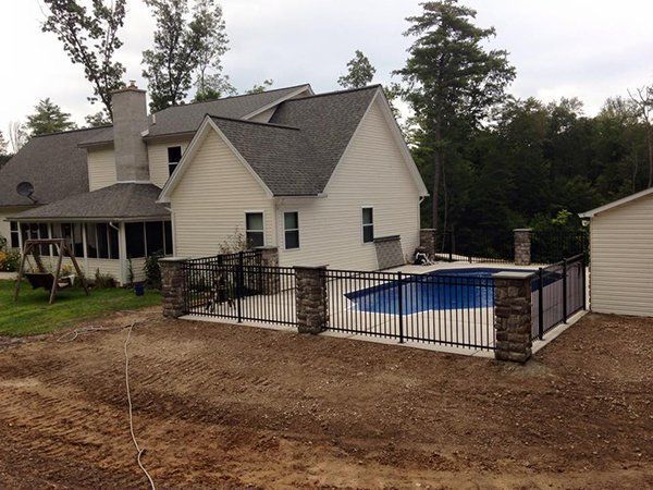 House with fenced backyard and a covered swimming pool beside a detached garage, surrounded by trees.