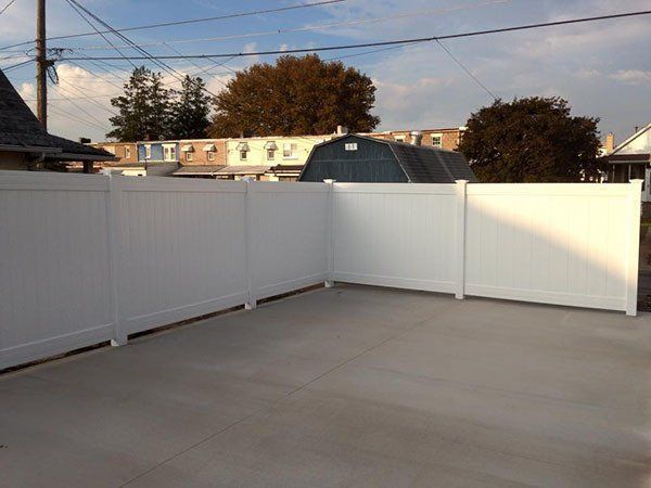 Empty concrete patio enclosed by white privacy fencing under a clear sky