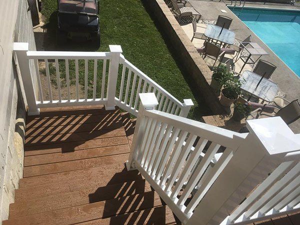 Wooden staircase with white railings beside a pool and patio chairs.