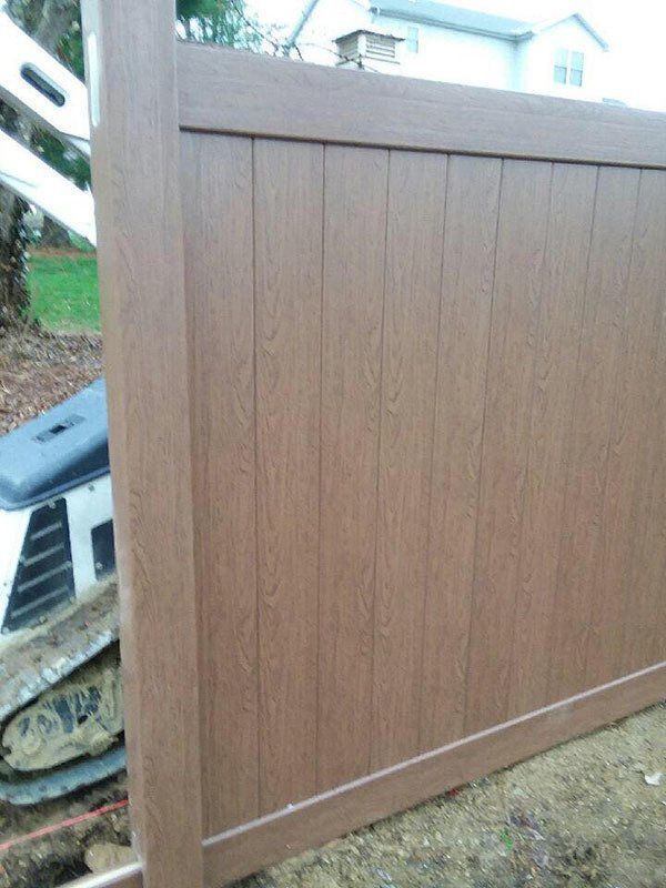 Brown wooden fence panel installed outdoors beside a house and steps