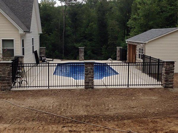 Backyard pool area with a blue-covered pool behind a black metal fence between two houses.