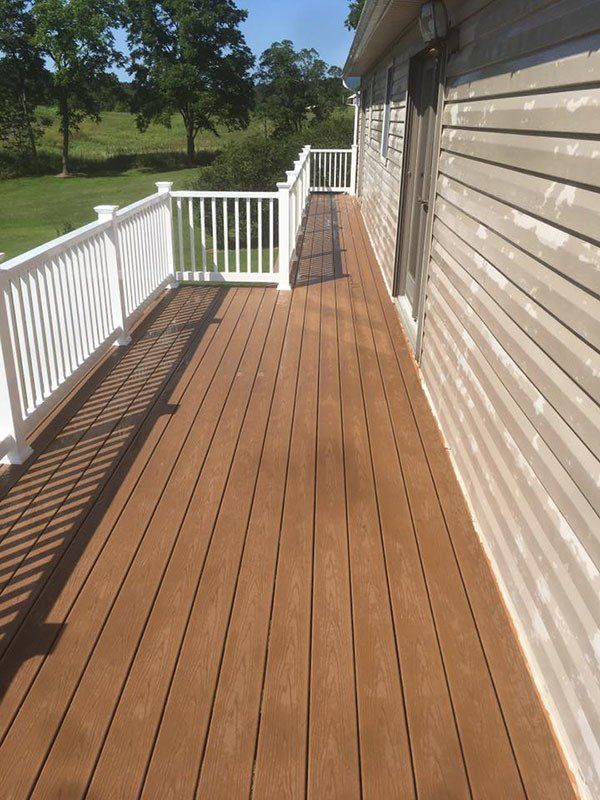 Wooden deck beside a house with white railings and a grassy yard in sunlight