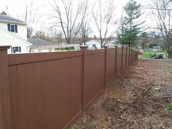 Long brown wooden privacy fence along a yard beside bare trees and neighboring houses.