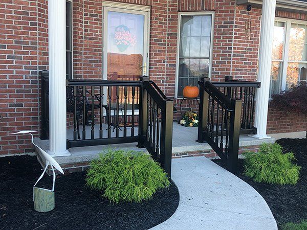 Brick house front porch with white columns, black railings, curved walkway, and pumpkins by the door