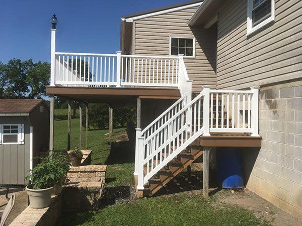 Backyard deck and staircase with white railings attached to a beige house, with a potted plant nearby.