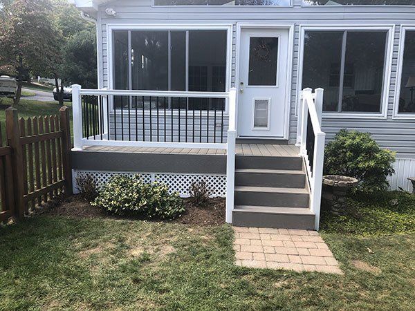 Front porch with white railings, steps, and a screened entry on a small house with a lawn and stone path.