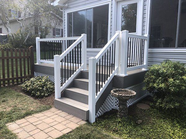 White front porch with stairs, railings, and sliding glass doors beside a small brick path and yard
