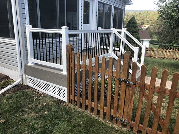 House porch with white railing and black mesh, next to a leaning wooden fence and gate at the side yard