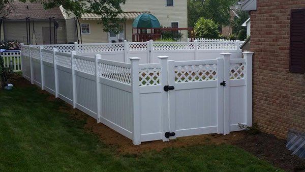 White vinyl fence with lattice trim enclosing a grassy yard beside a brick house.