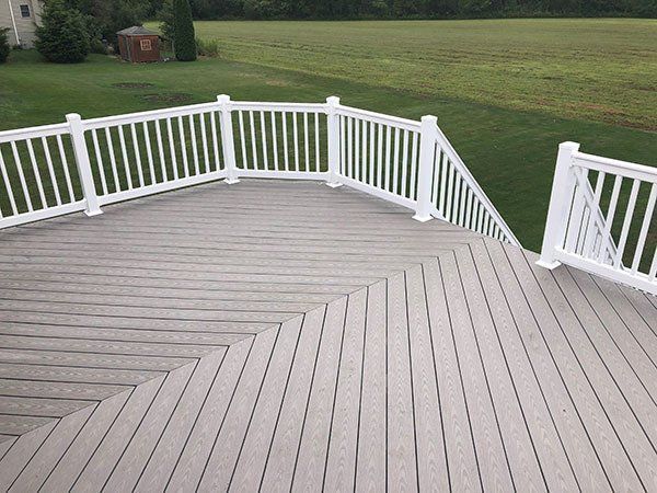 White wooden deck with railings overlooking a green lawn and a small shed