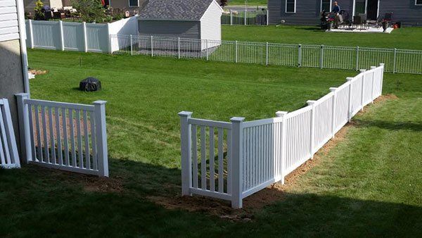 White vinyl fence enclosing a green backyard with a gate open in the foreground