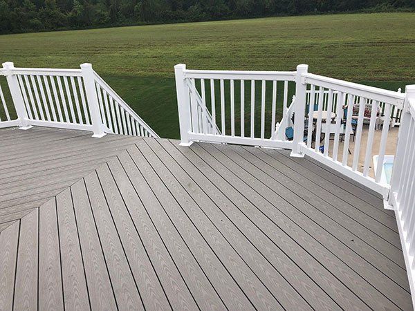 Gray deck with white railings overlooking a grassy landscape.