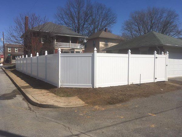 White vinyl privacy fence enclosing a corner yard beside a residential street under a clear blue sky