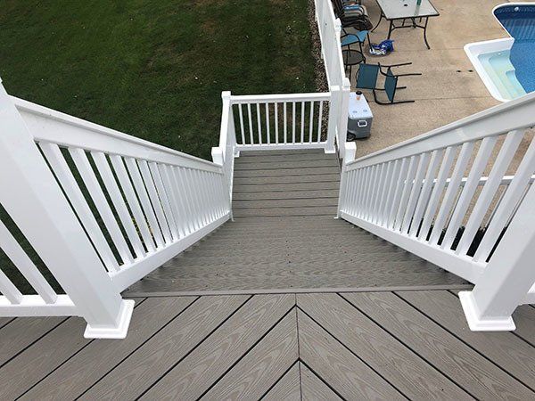 White staircase descending to a backyard deck and pool area, with gray wood steps and railings.