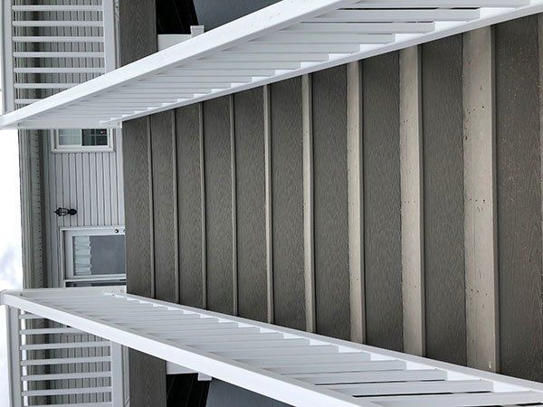 Covered stairway beside a gray building, viewed upward with white railings and metal roof panels