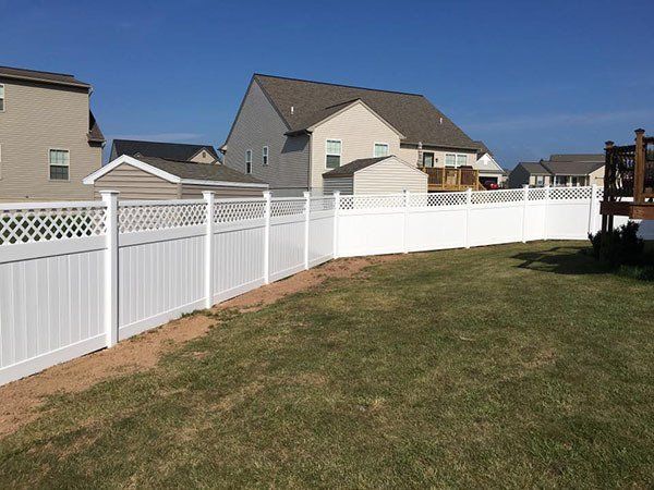 Curved white vinyl fence beside a grassy yard with suburban houses under a clear blue sky