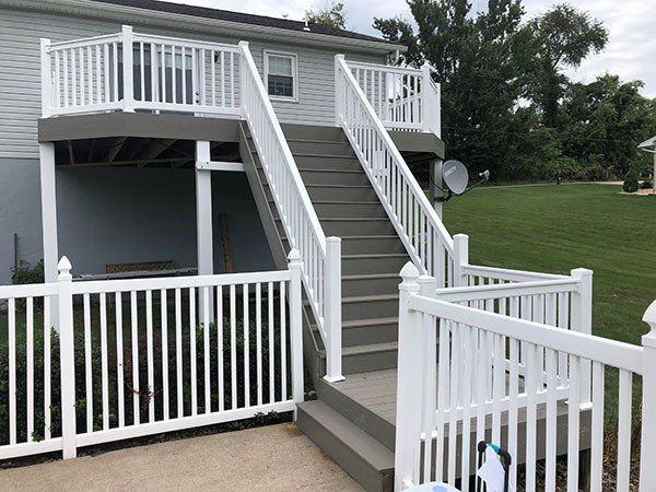 Elevated gray house with white railings, stairs, and a fenced porch in a grassy yard