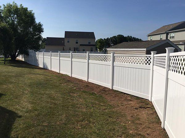 White vinyl fence along a grassy yard beside suburban homes under a clear blue sky