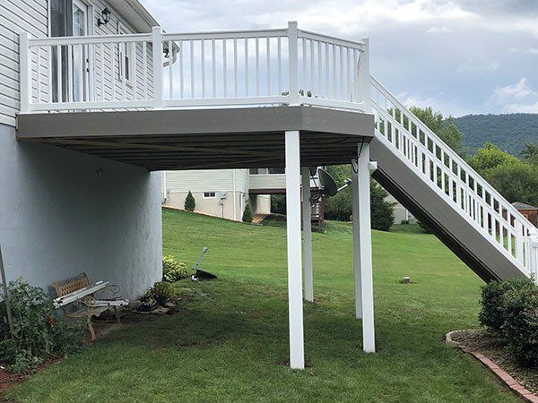 Raised deck with white railings and stairs over a grassy yard beside a house.