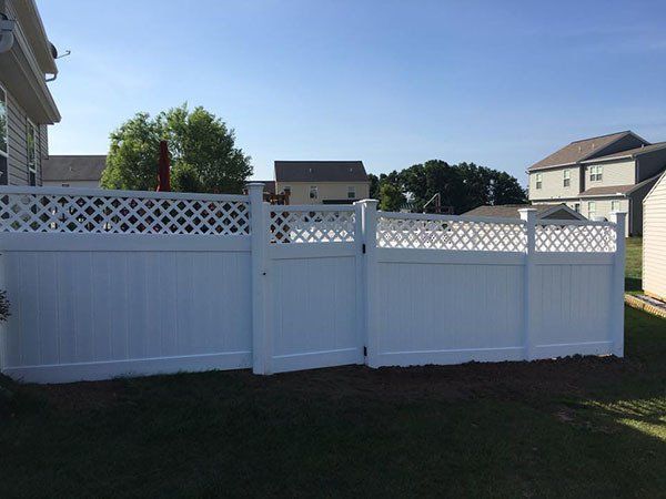 White vinyl backyard fence with lattice top in a suburban yard on a sunny day